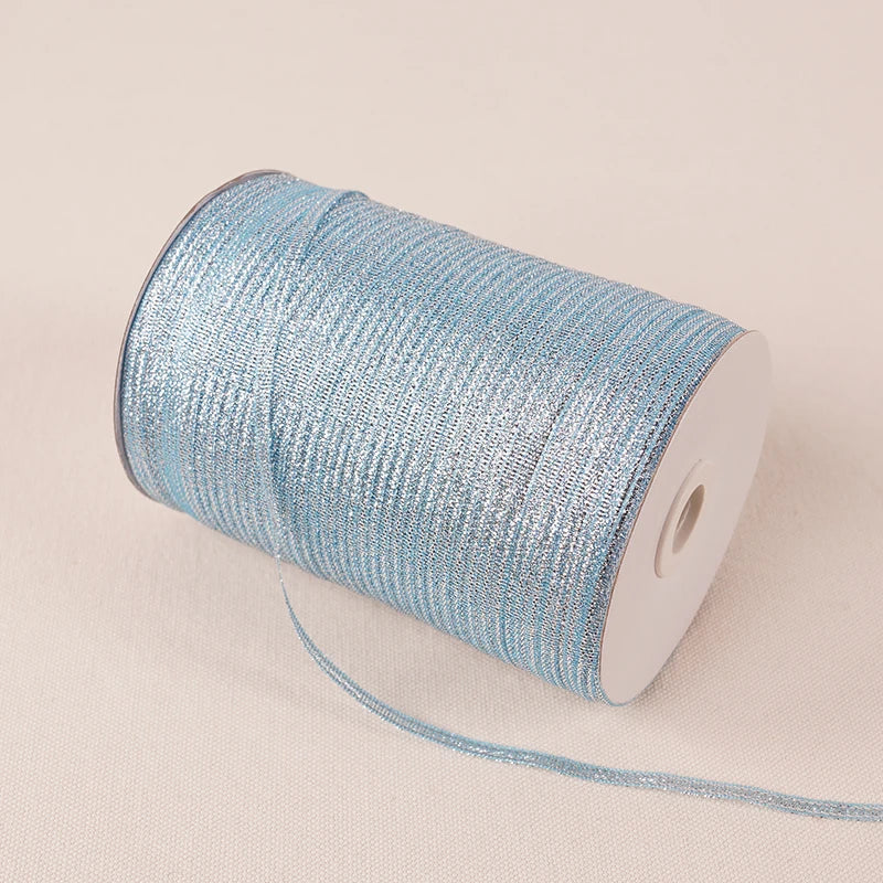 A roll of 10-meter gold and silver glitter satin ribbon with a white core lying on a light fabric.