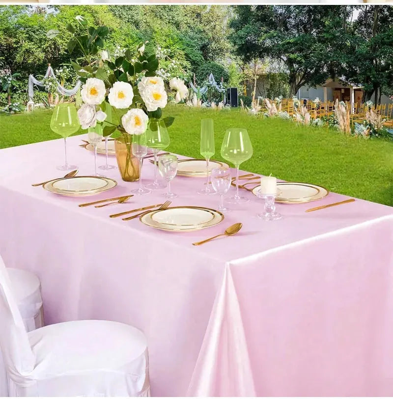 A pink satin tablecloth set for outdoor dining featuring gold plates, silverware, and clear glassware.