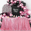 A pink sequin rectangle table cover is displayed with a backdrop of pink and black balloons and a chalkboard sign.