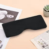 A black contoured travel sleep mask with a neck pillow is shown on a light background next to some papers and a succulent pla