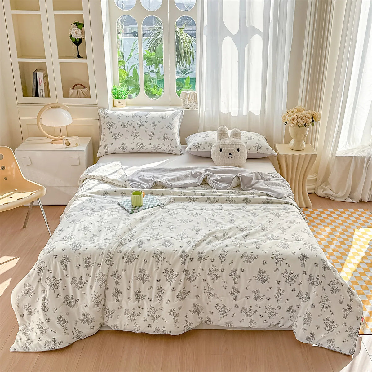 A light gray pastoral print quilt blanket is displayed on a bed with white bedding and decorative pillows.