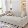 A light beige stretchable full-wrap sofa slipcover displayed in a modern living room setting.