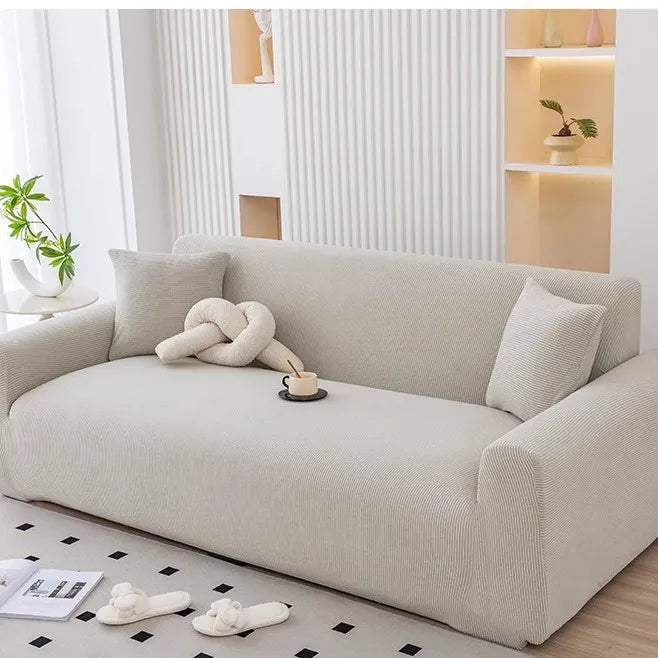 A light beige stretchable full-wrap sofa slipcover displayed in a modern living room setting.