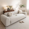 A white quilted sofa cover with elastic straps is displayed on a light-colored rug in a bright room.