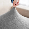 A hand is adjusting a gray waterproof jacquard stretch sofa cover on a piece of furniture.