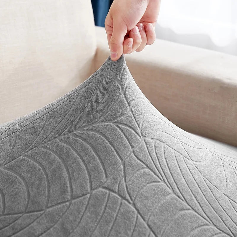 A hand is adjusting a gray waterproof jacquard stretch sofa cover on a piece of furniture.