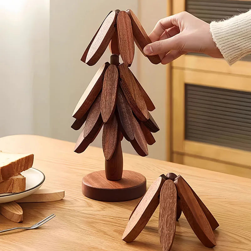 A hand holds an insulated wooden placemat shaped like a stylized tree, resting on a wooden table.