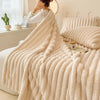 A thick, cream-colored, vertically striped flannel blanket draped over a bed, with a person in a white top standing nearby.