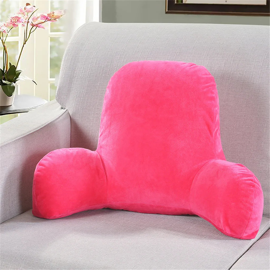 A bright pink plush lumbar support cushion with arms resting on a light gray sofa.