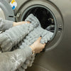 A person's hands are pulling a thick gray flannel sofa pad cover out of a washing machine drum.