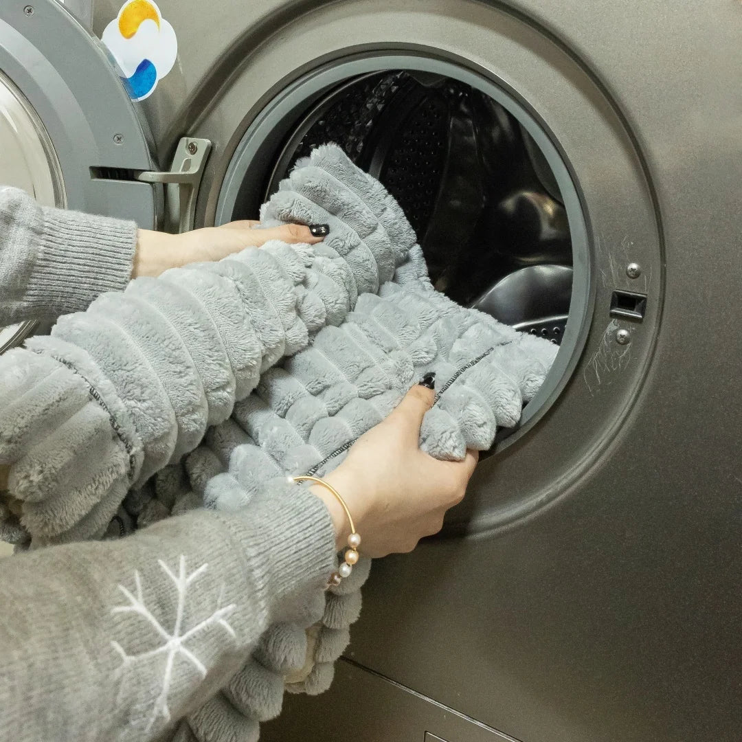 A person's hands are pulling a thick gray flannel sofa pad cover out of a washing machine drum.