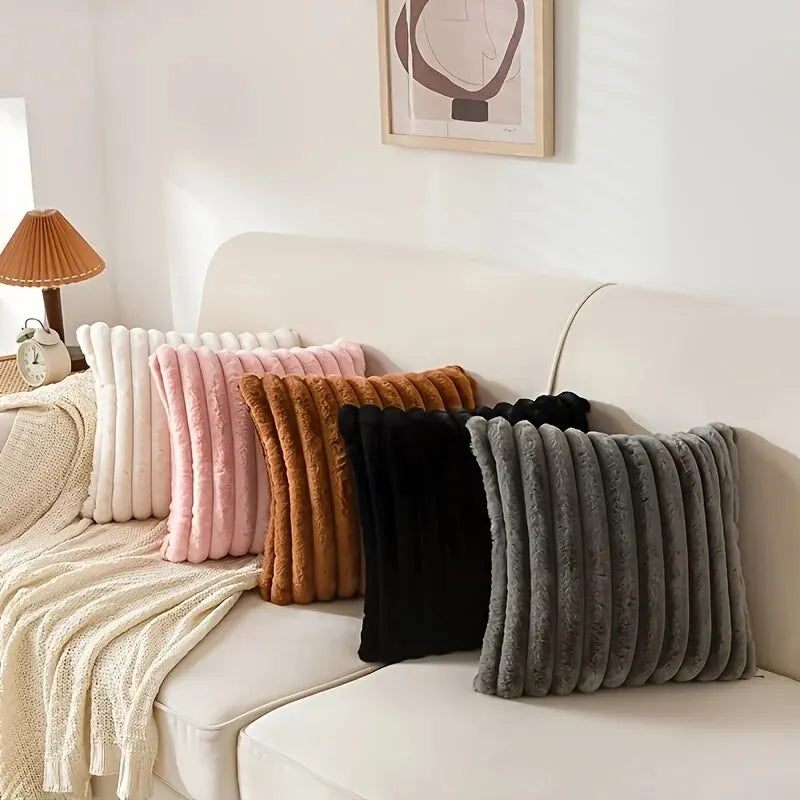 A collection of striped corduroy pillow covers in shades of pink, beige, brown, and black displayed on a white sofa.
