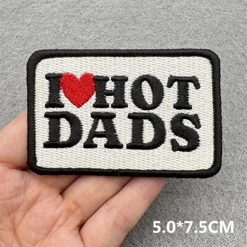 Black and white embroidered patch with the text I HOT DADS and a red heart on a gray background