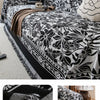 A black and white floral jacquard sofa throw blanket draped over a sofa, featuring intricate botanical patterns.