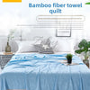 A light blue bamboo fiber towel quilt draped over a bed with white pillows and green plants.