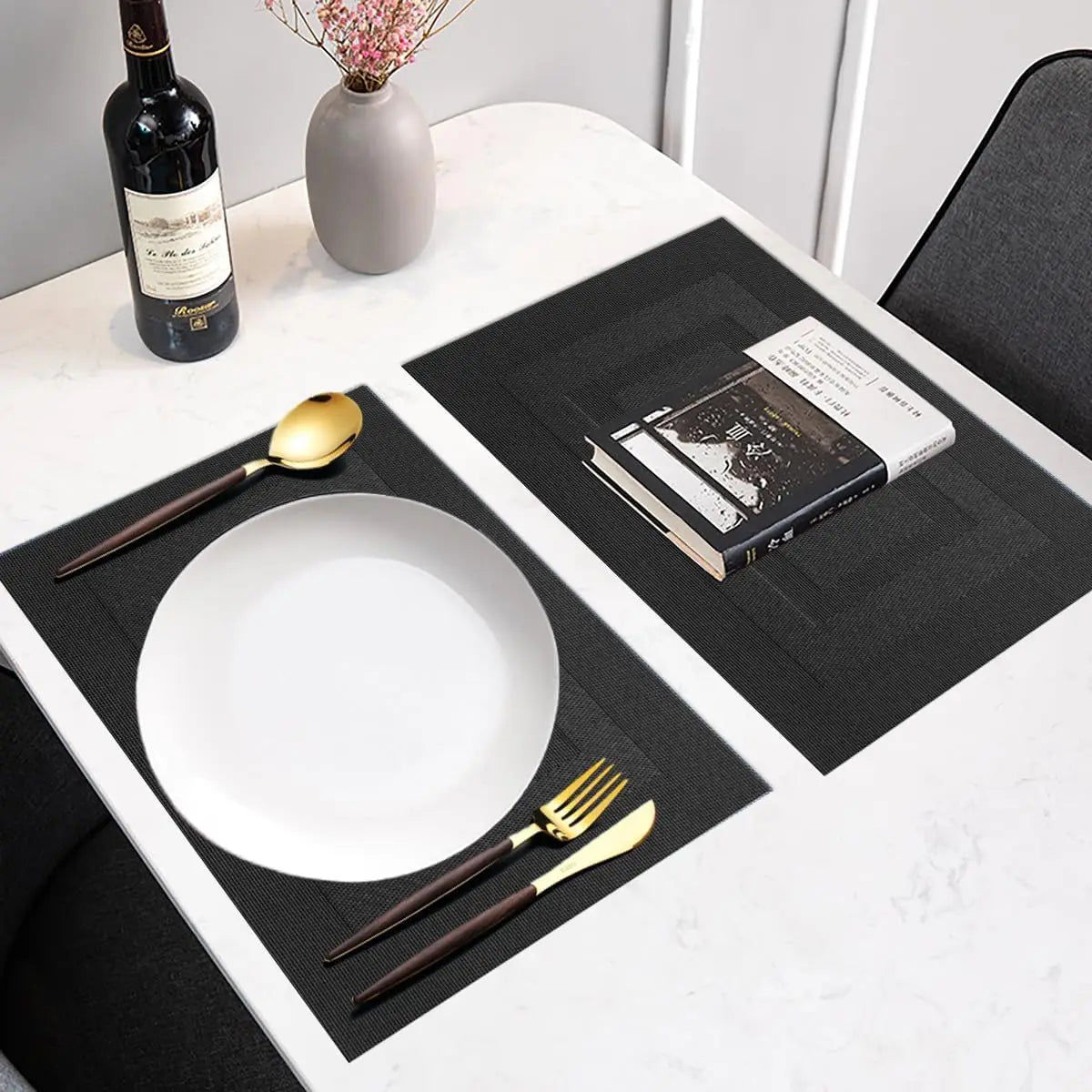 A set of six black non-slip heat resistant placemats is displayed on a white table with tableware and a bottle of wine.