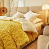 A bright yellow quilted fleece blanket draped over a beige bed with white pillows and natural light.