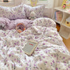 A white and purple floral duvet cover set with matching pillowcases and a decorative quilted cover is displayed on a bed.
