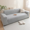 A light gray Jacquard velvet sofa cover displayed on a modern sofa with white pillows and a small tray.