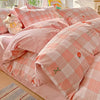 A pink plaid duvet and pillow set with orange accents and a small stuffed animal on a bed.
