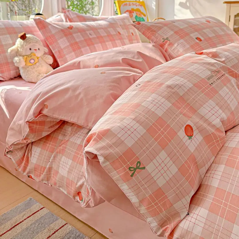 A pink plaid duvet and pillow set with orange accents and a small stuffed animal on a bed.