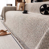A beige chenille sofa cover draped over a sofa, with brown and cream pillows and a black mug on the surface.
