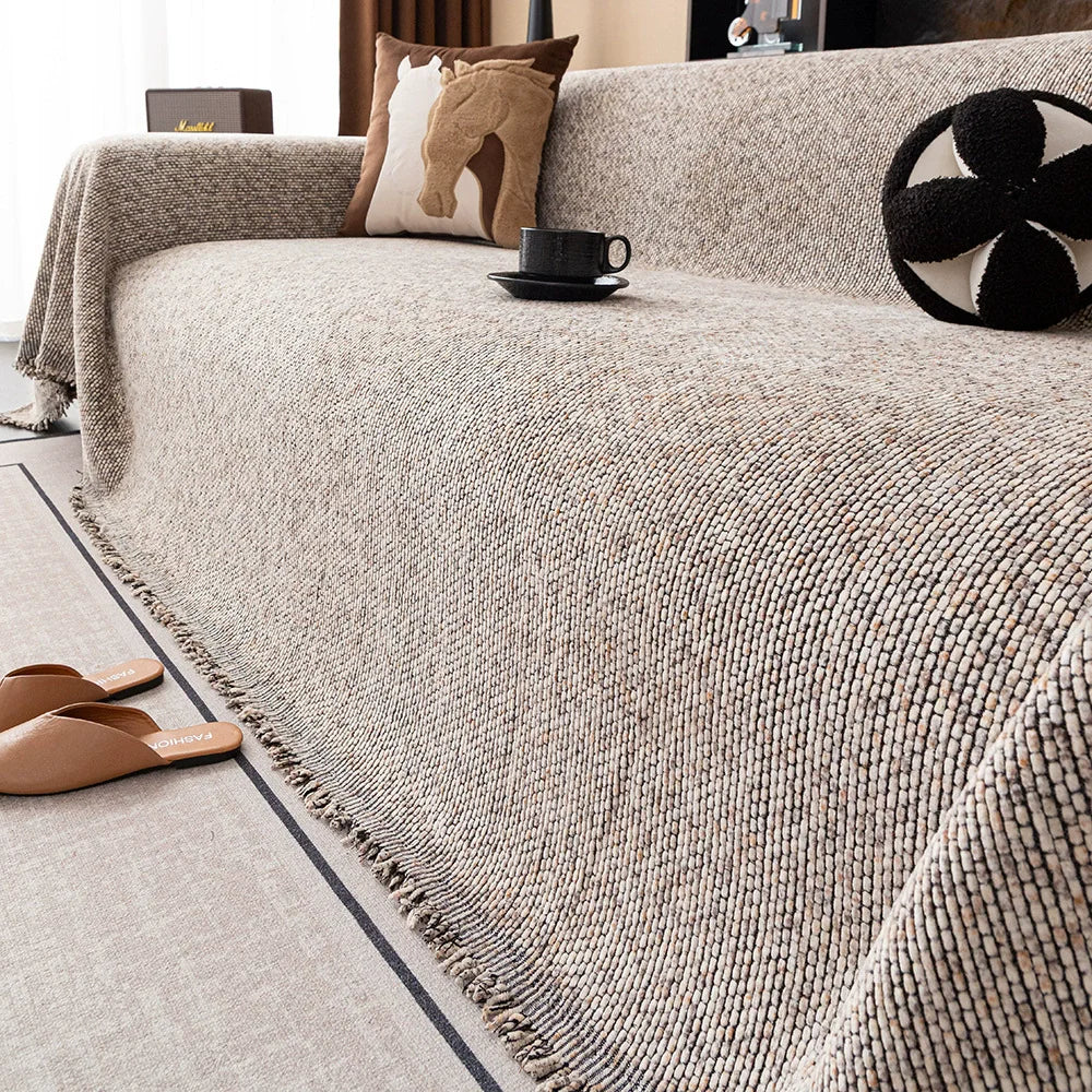 A beige chenille sofa cover draped over a sofa, with brown and cream pillows and a black mug on the surface.