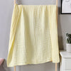 A yellow ultra-soft 100% cotton gauze blanket hanging on a wooden rack.
