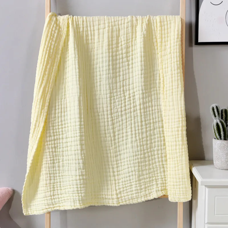A yellow ultra-soft 100% cotton gauze blanket hanging on a wooden rack.