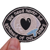 Black embroidered patch with white text and a black heart design that reads We need never be ashamed of our tears