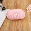 A pink flat thread yarn skein lying on a wooden surface next to a glass bottle and a rose flower.