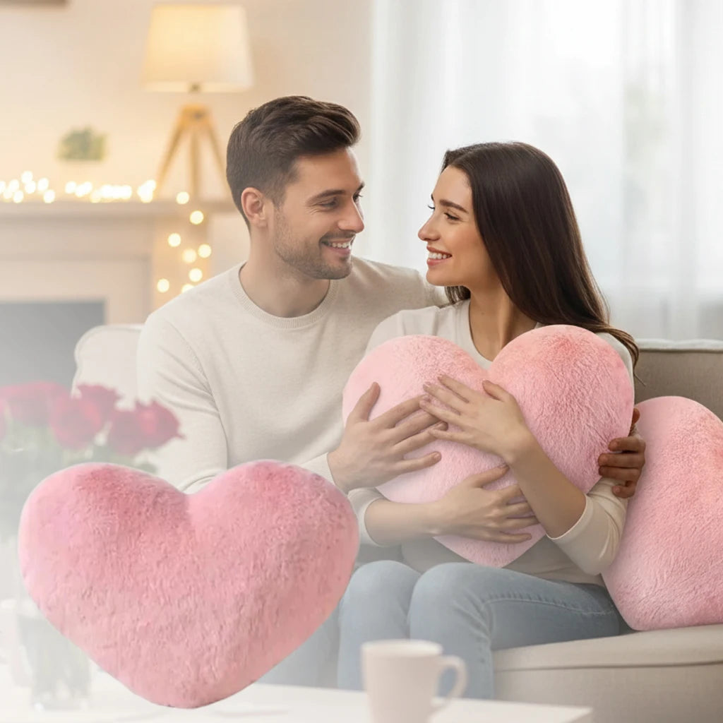 A woman is holding a pink heart-shaped plush cushion while sitting on a couch.