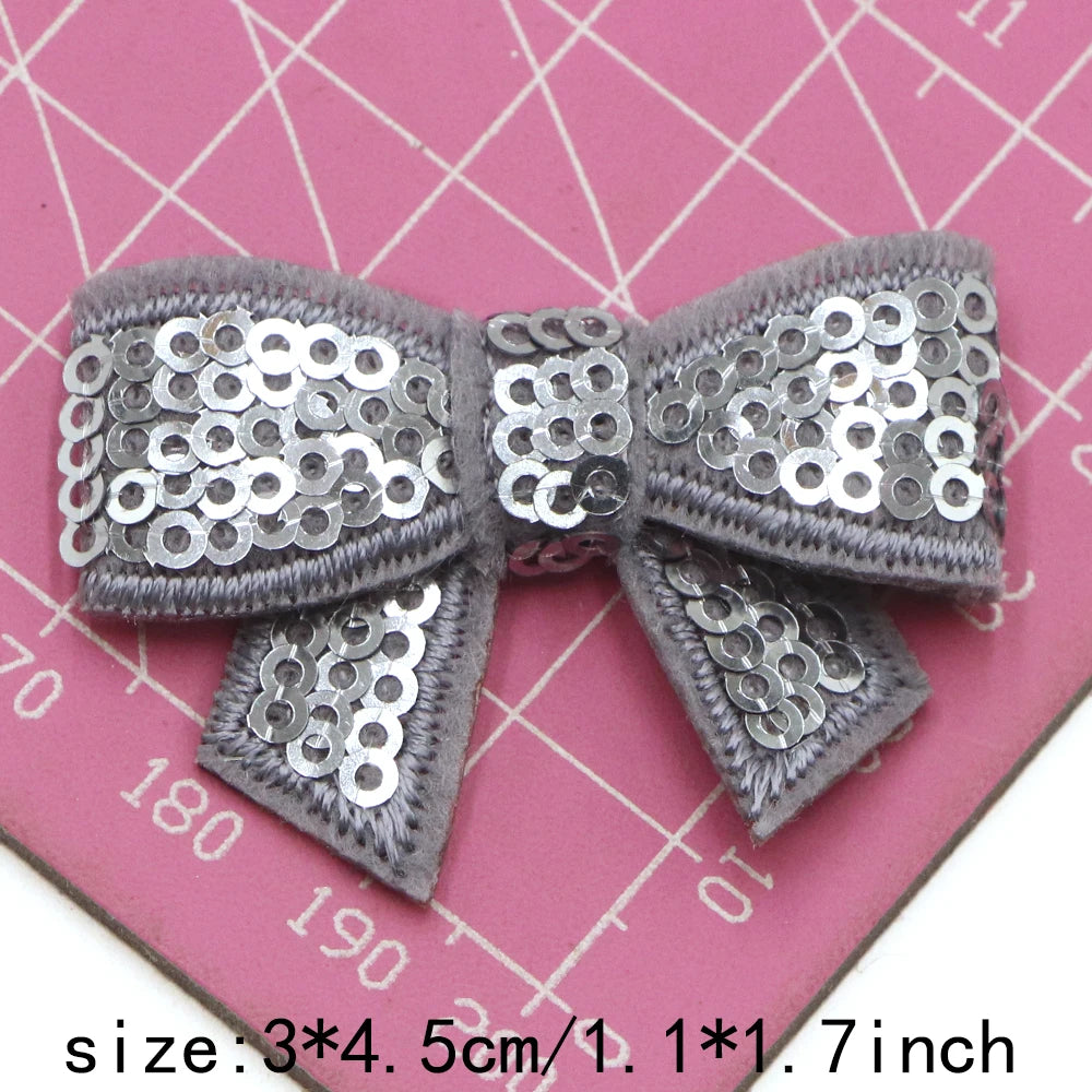 Silver sequin bow patches for DIY decoration shown on a pink ruler.