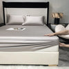 A luxury bed with a fitted sheet and pillows in silver-gray tones, featuring a dark headboard and modern decor.