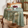A round table set with a green floral lace tablecloth, a white lamp, and a bowl of red berries.