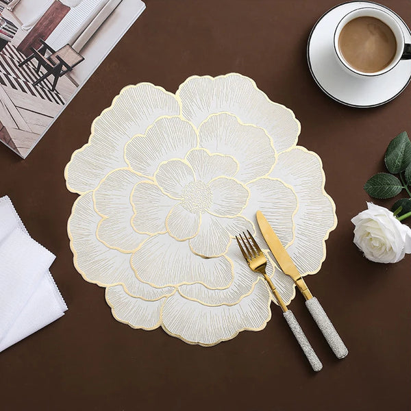 Gold plated peony coasters on a dark brown surface with a white napkin and a cup of coffee.