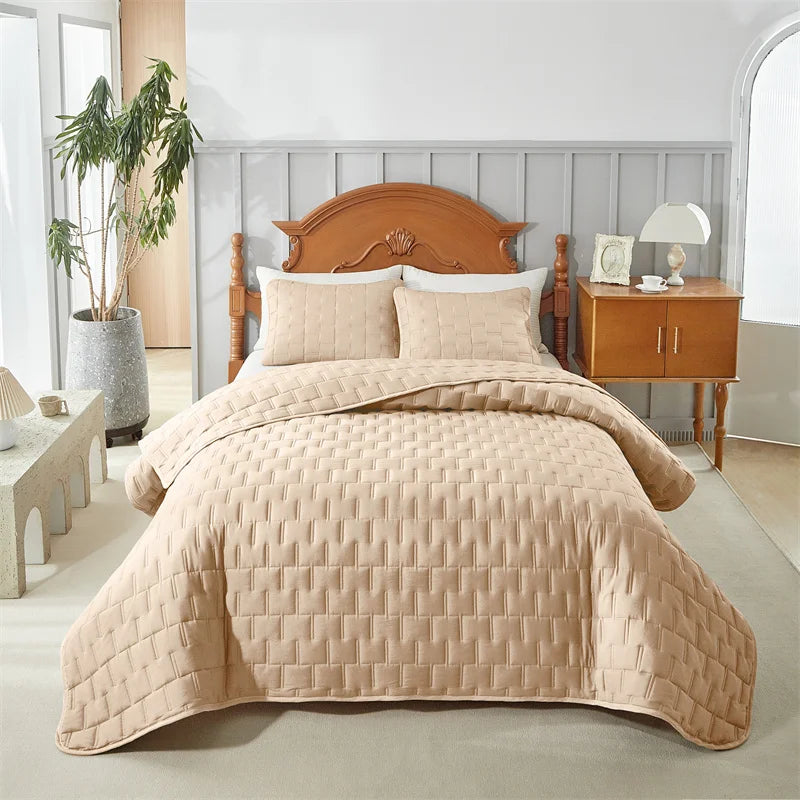 A light beige quilted bedding set with a wooden headboard and bedside table in a bright bedroom.