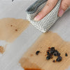 A hand is using a reusable silicone liner to clean spills on a paper towel, demonstrating easy cleaning.