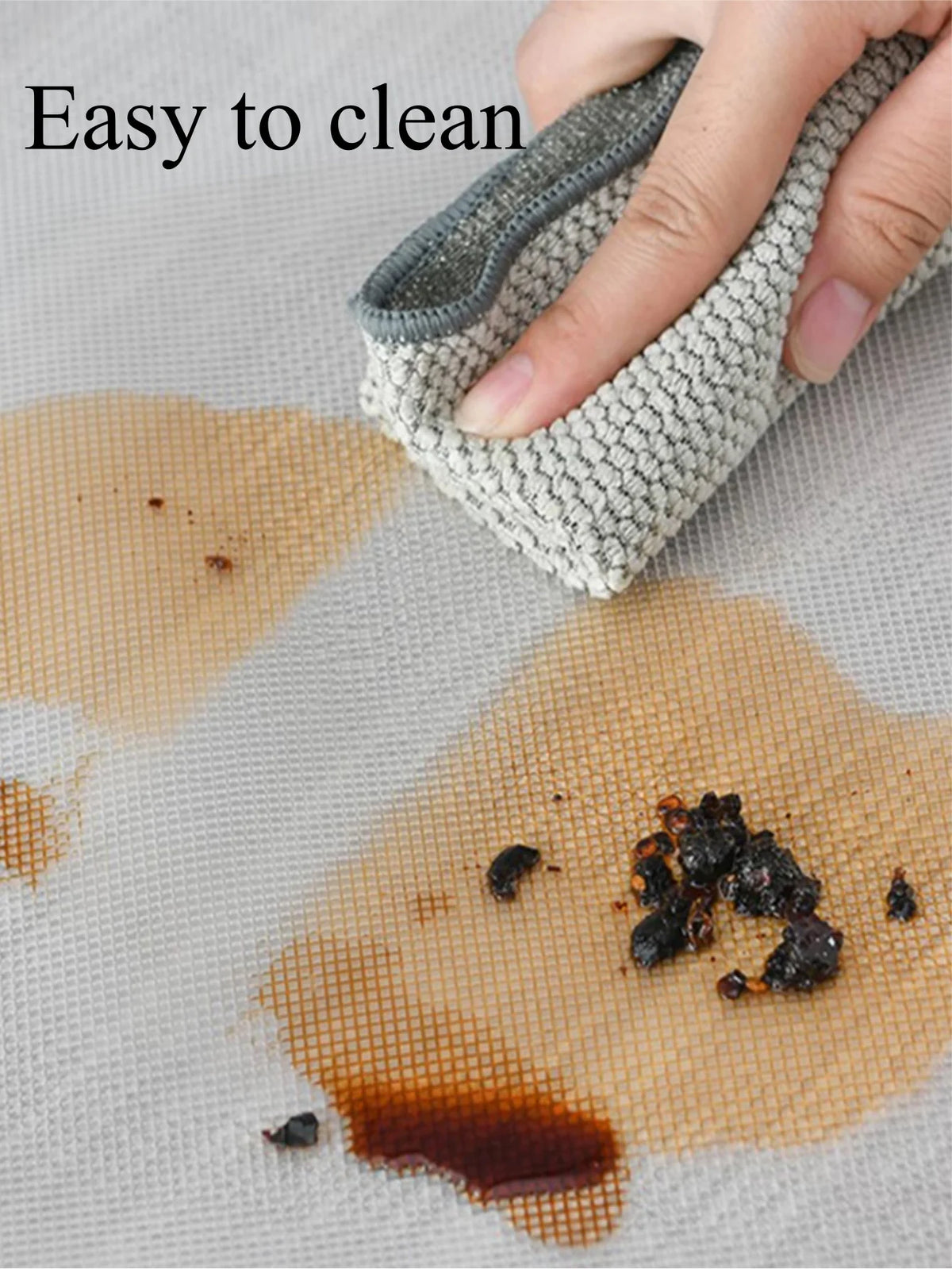 A hand is using a reusable silicone liner to clean spills on a paper towel, demonstrating easy cleaning.