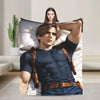 A man with light brown hair wearing a dark blue shirt and jeans is lying on a white throw blanket, holding it up while a woma