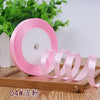 Pink satin ribbon roll with several coiled ribbons displayed on a wooden surface.