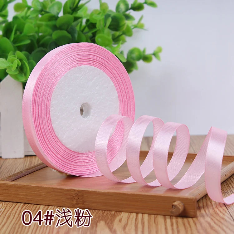 Pink satin ribbon roll with several coiled ribbons displayed on a wooden surface.