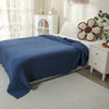 A navy blue gauzy blanket draped over a white bed with a cream-colored wooden nightstand and decorative pillows.