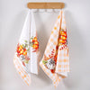 A set of two kitchen towels featuring a pumpkin and plaid design hanging on a wooden rack.