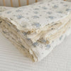 A stack of white muslin blankets with a blue floral print and delicate lace trim.
