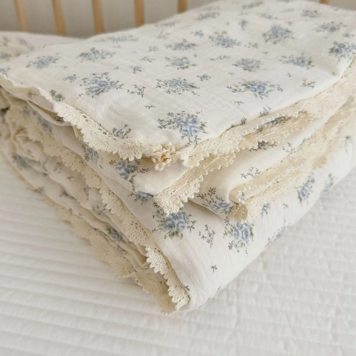 A stack of white muslin blankets with a blue floral print and delicate lace trim.
