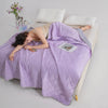 A person is lying down under a purple breathable cooling blanket on a white surface.