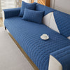 A deep blue quilted anti-slip sofa cover with a plush texture on a white sofa.