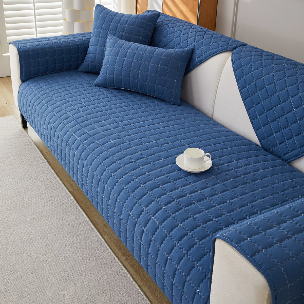 A deep blue quilted anti-slip sofa cover with a plush texture on a white sofa.