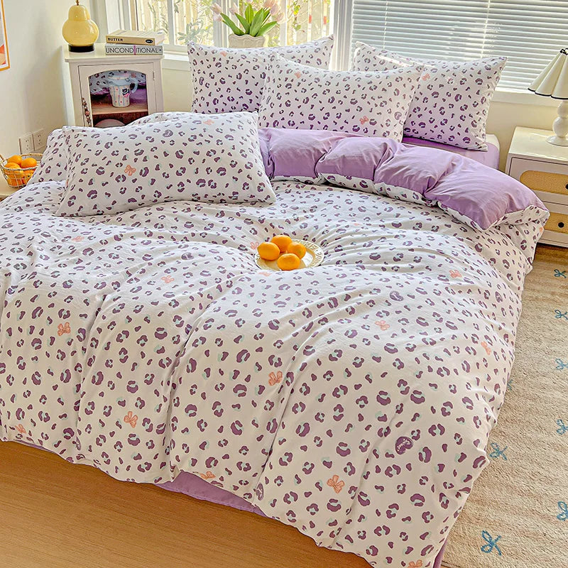 A purple and white floral printed bedding set featuring patterned pillows and a duvet on a bed.